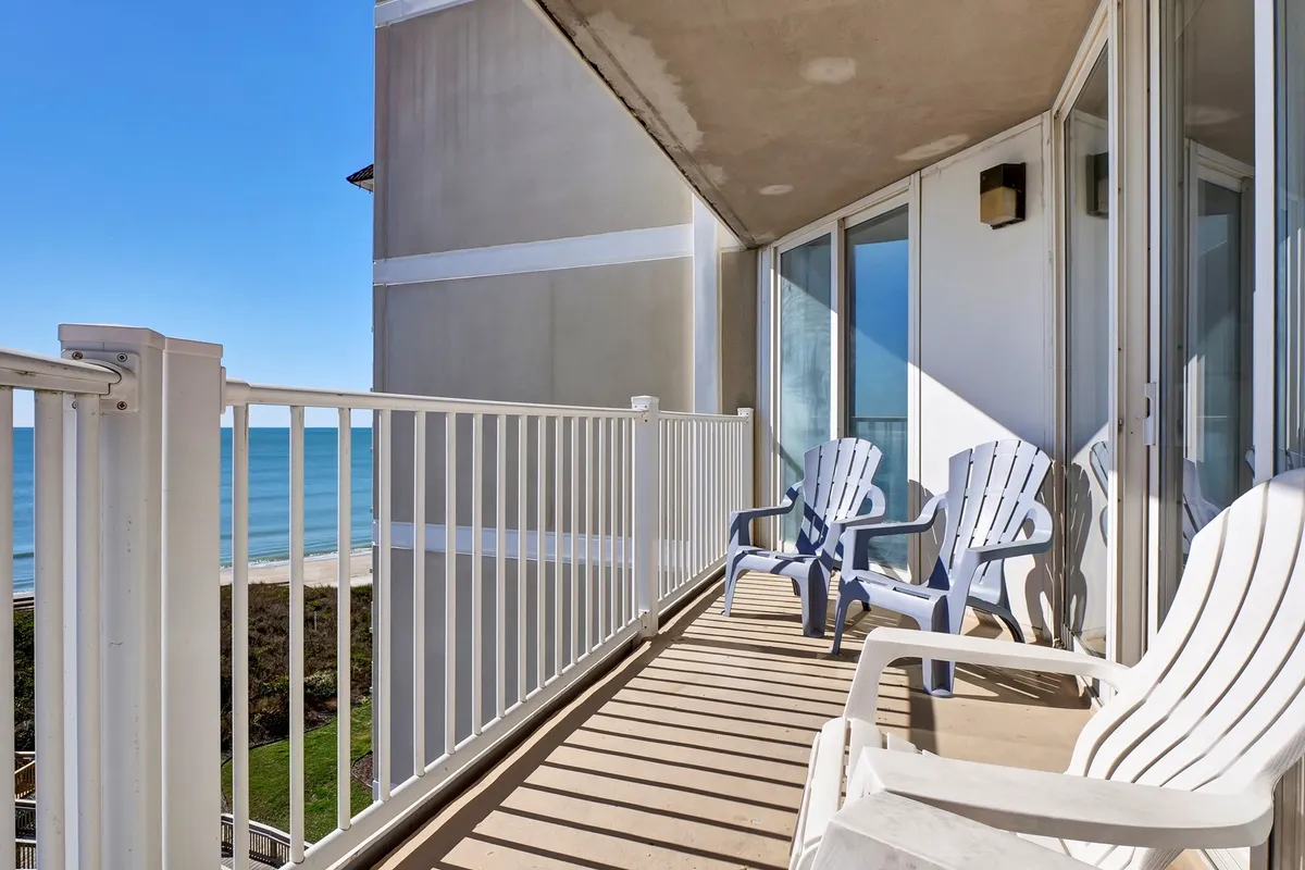 A serene private balcony featuring comfortable chairs and railings with an unobstructed ocean view. The space is perfect for relaxing, reading, or simply soaking in the sunrise with a cup of coffee. The tranquil mood complements the peaceful coastal lifestyle described in the section.