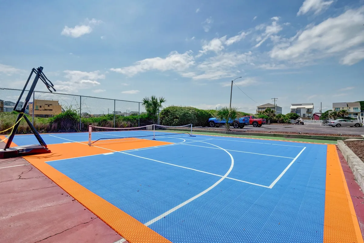 This energetic exterior shot centers on a colorful basketball/pickleball sports court set amidst greenery. The court’s bright colors and inviting layout suggest friendly competitions and active play, supporting the theme of all-ages adventure.