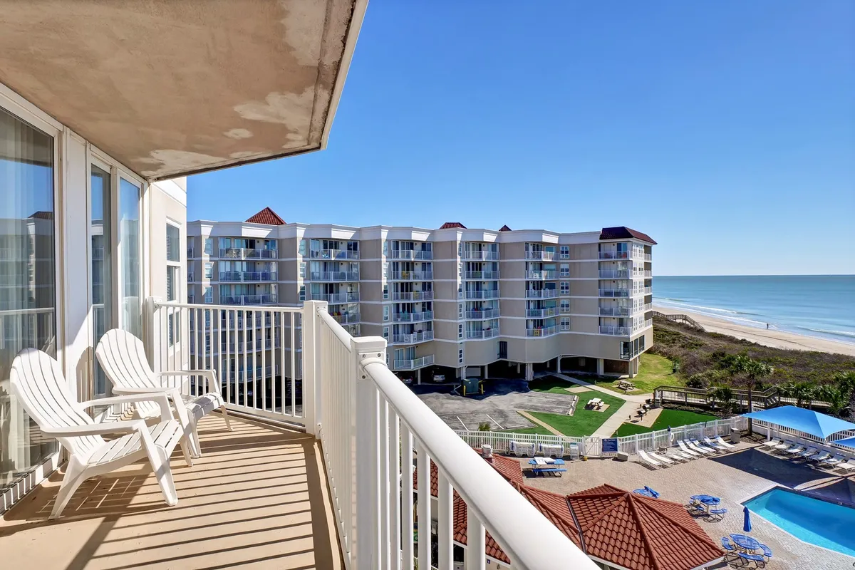 This exterior scene features a private balcony with comfortable chairs overlooking the Atlantic Ocean and the pool area below. The building’s architecture frames the tranquil water views, inviting guests to relax and soak in the sunrise or enjoy quiet evenings. The pool area and beach access are visible, tying together the key amenities described in the section.