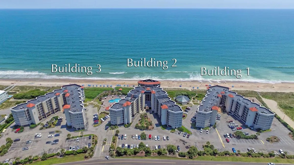 An exterior image showing three resort buildings with distinct architecture, a spacious swimming pool area, and close proximity to the sandy beach. The scene exudes a leisure-oriented mood, with the pool and ocean serving as central attractions for couples and small groups seeking both relaxation and fun.