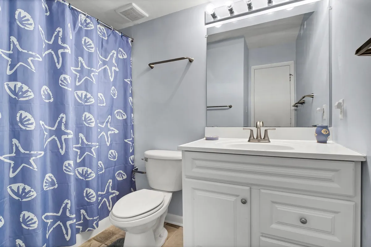 A fresh, inviting bathroom decorated with a starfish-patterned shower curtain, a white vanity, mirror, and modern light fixtures. The space feels clean and coastal, evoking relaxation and a beach-inspired vibe.