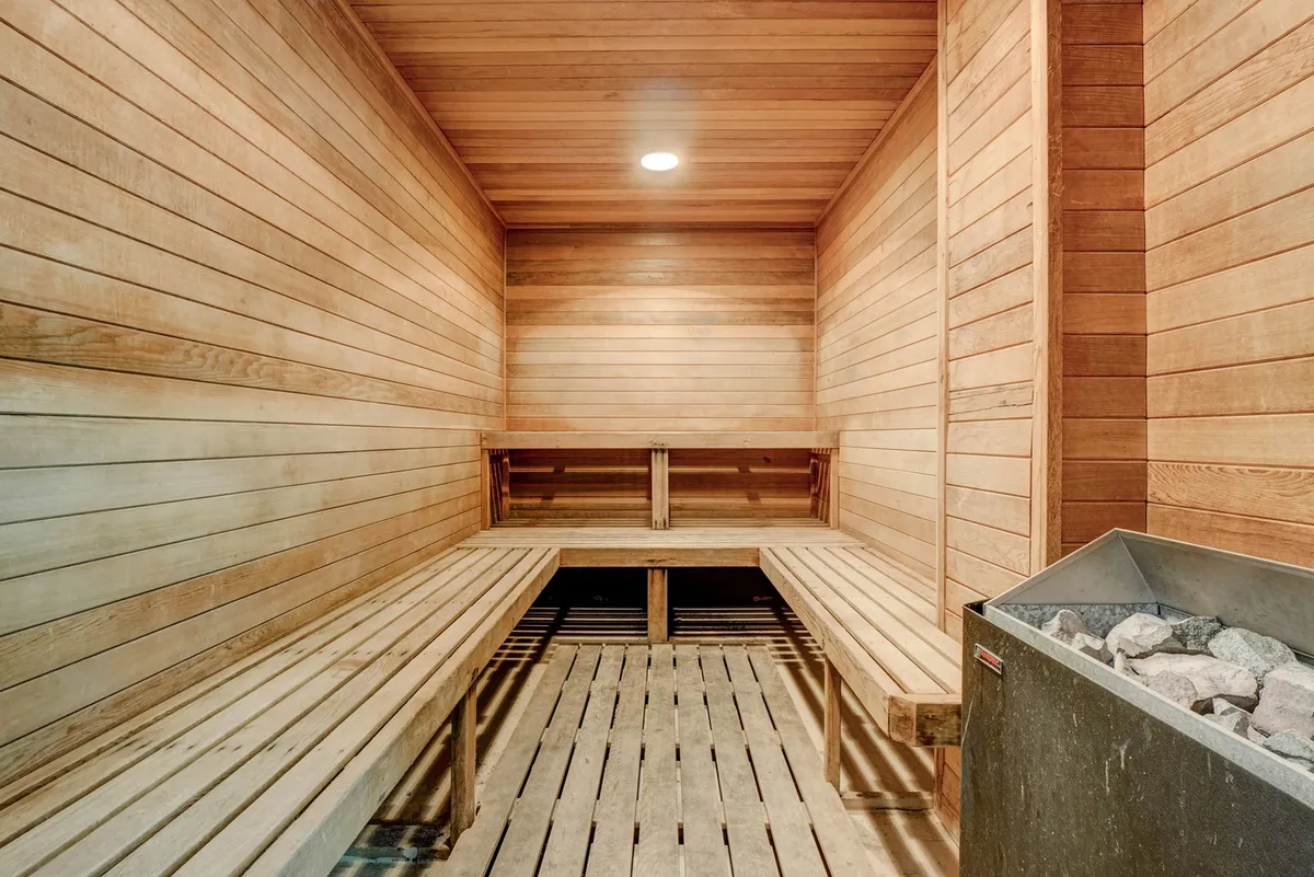 A tranquil sauna room with wooden benches, a stone heater, and warm wood paneling, creating an inviting environment for relaxation and recovery.